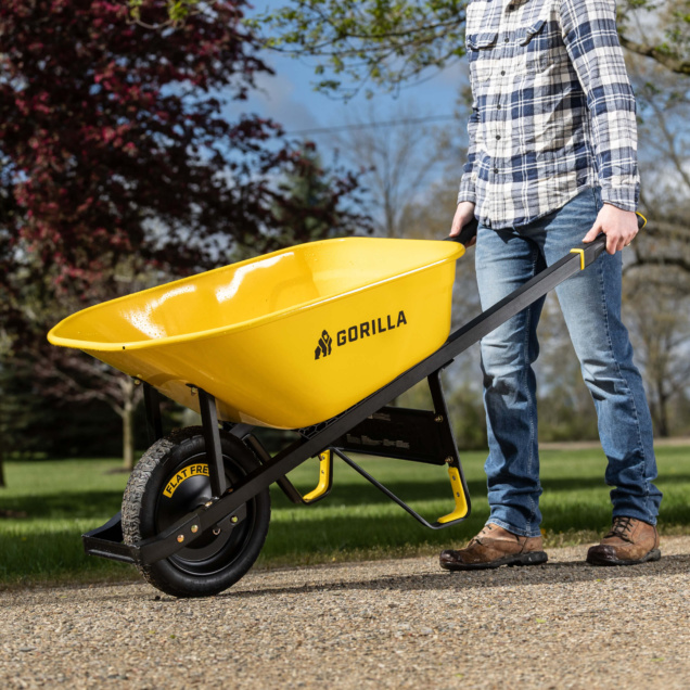 Yellow Gorilla wheelbarrow with "FLAT FREE" tire in use on gravel path.