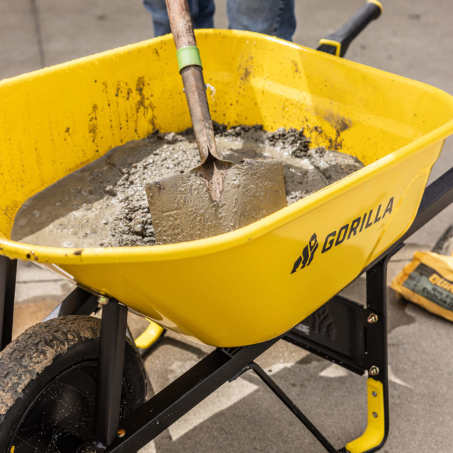 Yellow Gorilla wheelbarrow filled with concrete, shovel inside; outdoor use.