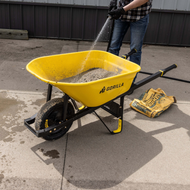 Yellow Gorilla wheelbarrow being filled with cement mix; bag labeled "QUIKRETE" nearby.