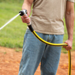 Person using a yellow and black Gorilla garden hose, spraying water outdoors.