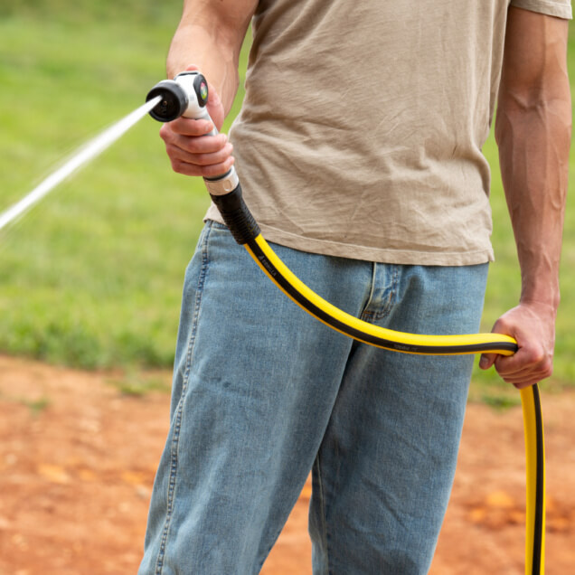 Person using a yellow and black Gorilla garden hose, spraying water outdoors.